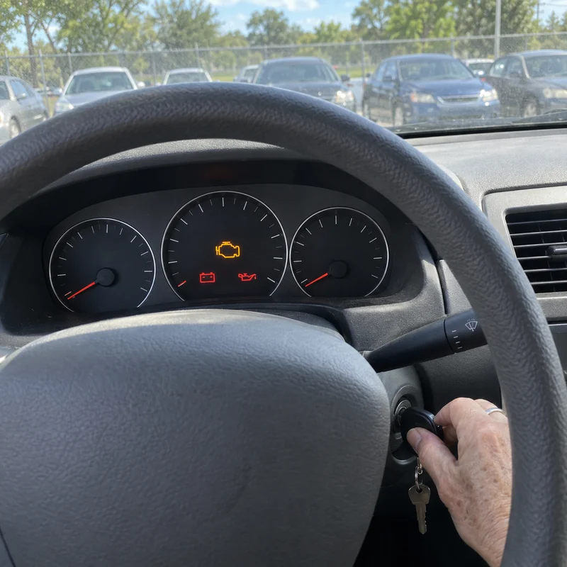 A hand turning the key on a used car, the engine light lit on the dash