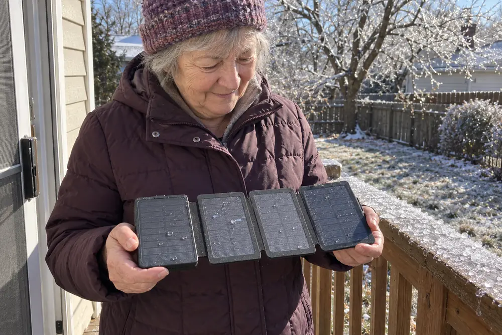 A woman in a winter coat on her back porch after a sleet storm, holding her open TerraCell in both hands, melt water beaded on its four panels in the morning sun