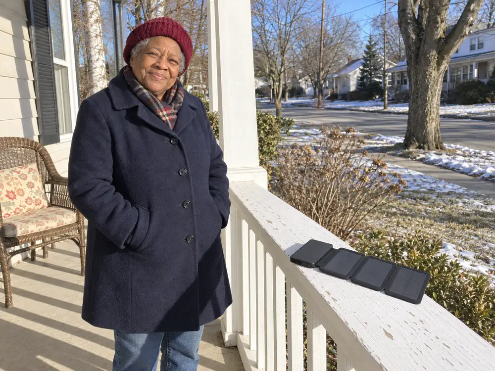 Bernice in her winter coat on her front porch, her TerraCell open on the porch rail in the sun