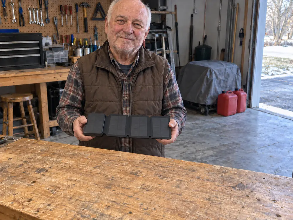 Harold at his garage workbench holding his open TerraCell in both hands, a covered generator and two gas cans behind him