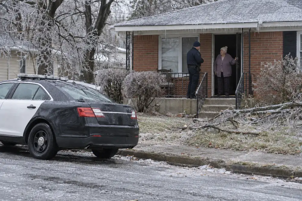 After an ice storm, a police officer on an older woman's porch, the woman in her dark doorway, a patrol car at the curb