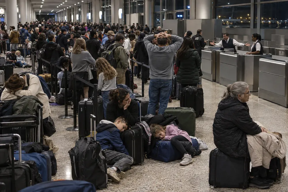 A crowded airport hall at night, stranded travelers waiting in a long line and sitting on the floor with their bags