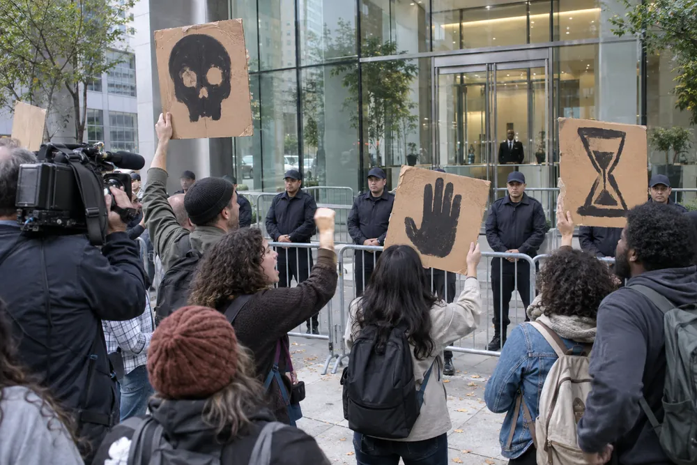 Protesters with hand-painted signs held back by a police line and barricades outside a tech company's glass headquarters