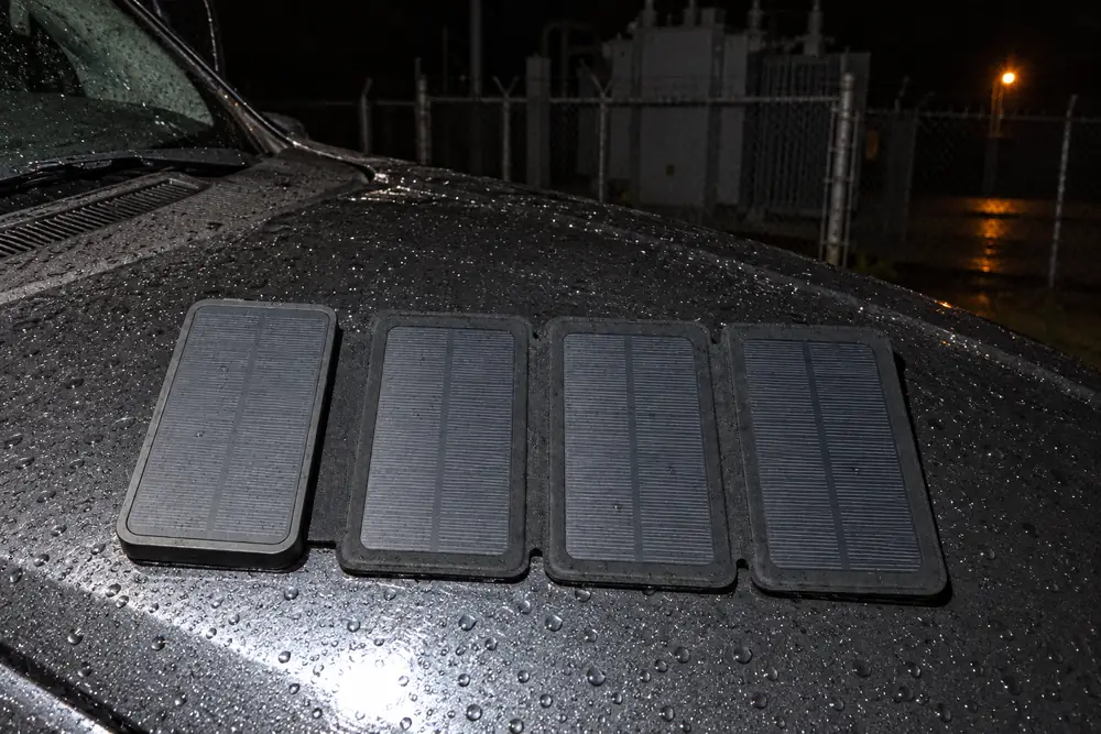 A flash photo at night: TerraCell opened flat on the wet hood of a pickup, its four solar panels in a row, the substation fence behind