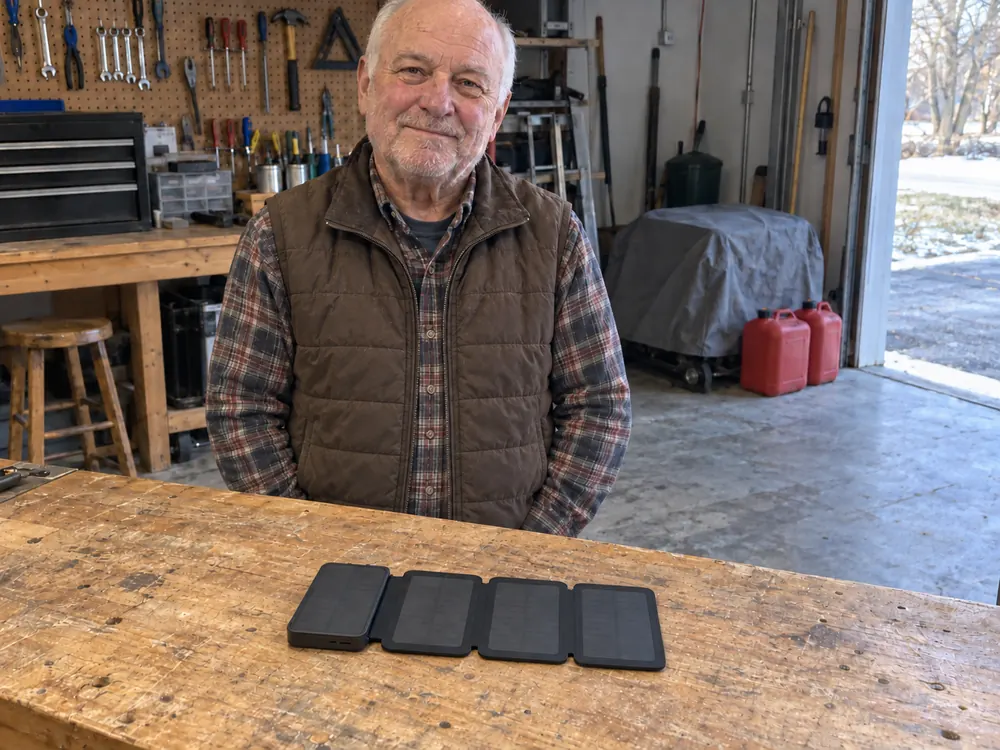 Harold at his garage workbench, hands in his pockets, a TerraCell open on the bench, a covered generator and two gas cans behind him