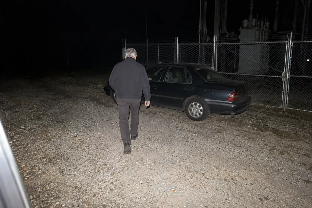 A flash photo at night: the silver-haired stranger walking back across the gravel to his old sedan parked by the substation fence
