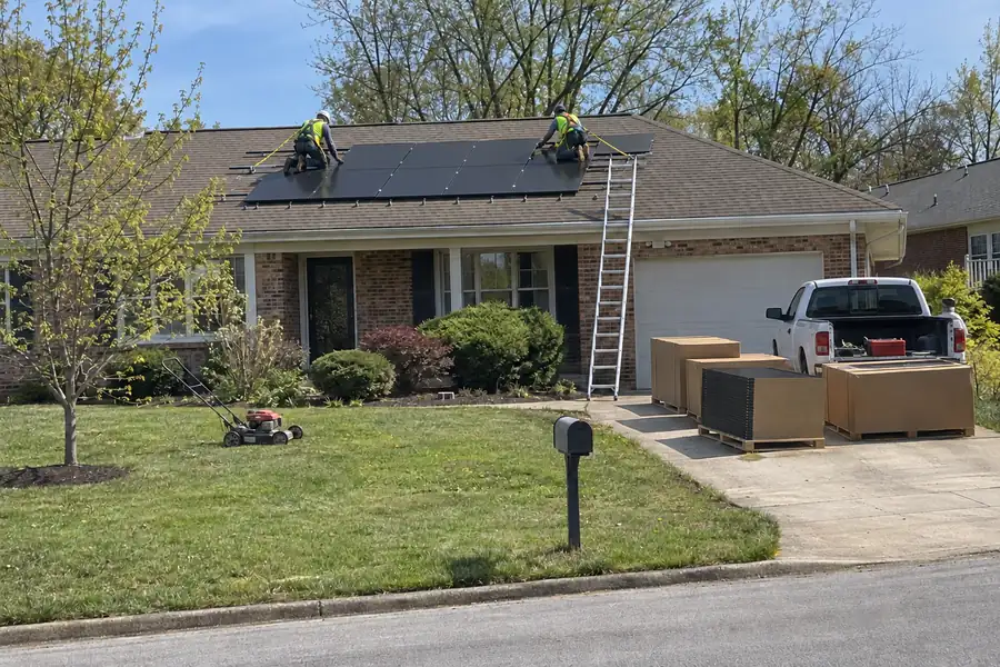 Installers bolting new solar panels onto a brick ranch house roof, seen from across the street