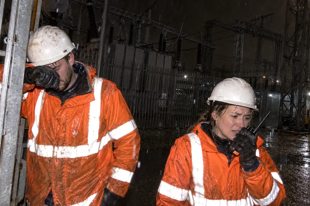 Two tired engineers at a substation at night in the rain