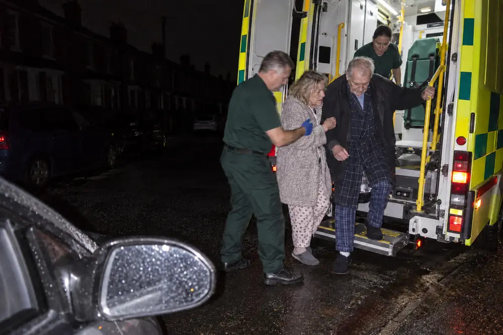 Paramedics helping an older couple from an ambulance on a dark street