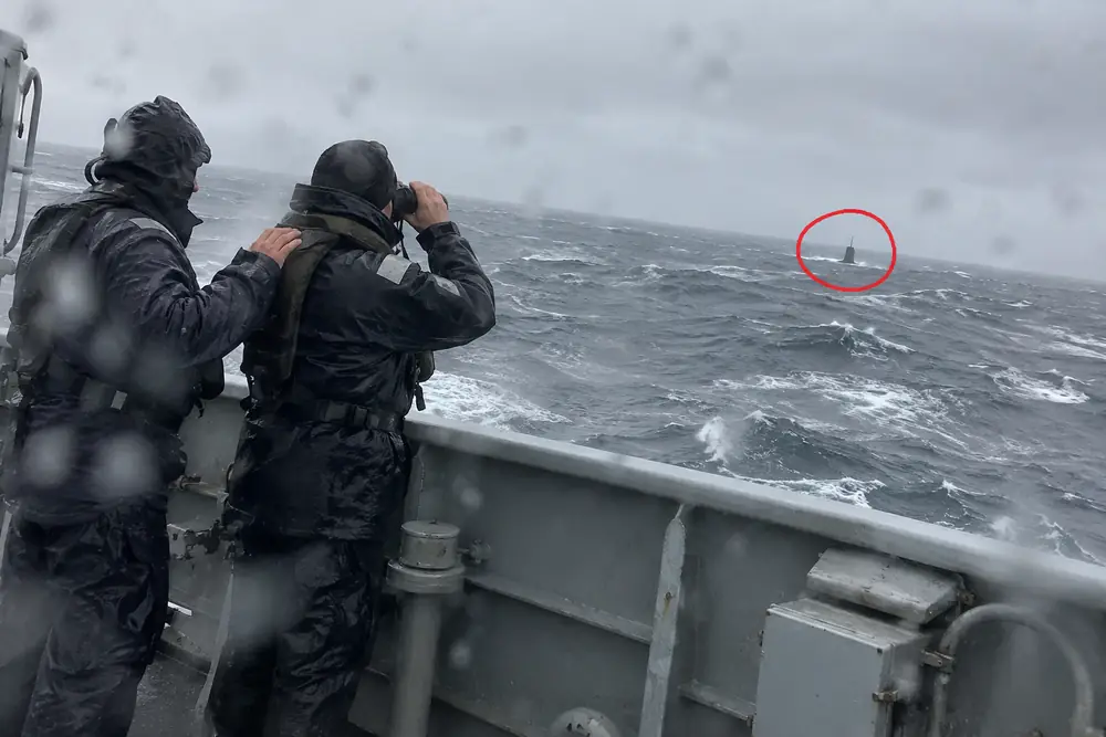 Sailors on a warship watching a submarine, circled in red