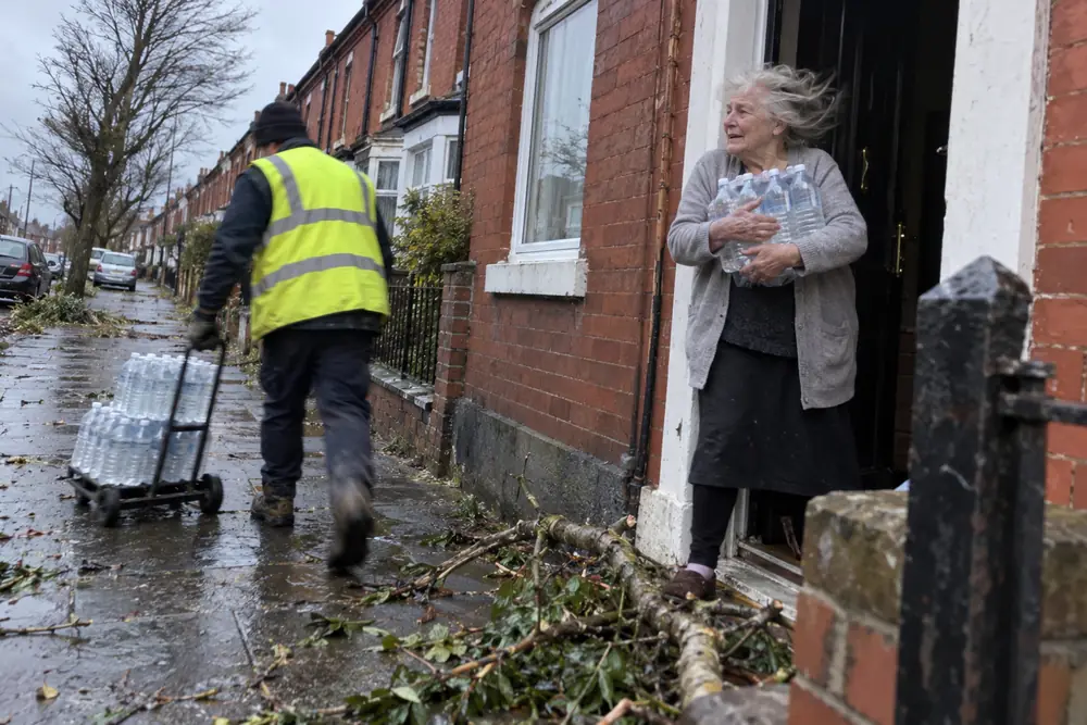 An older woman holding bottled water at her door after the storm