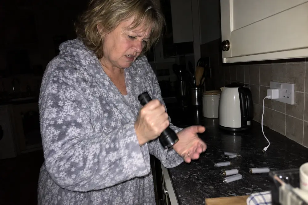 A woman in a dark kitchen with a dead torch, flat batteries and a charger in a dead socket