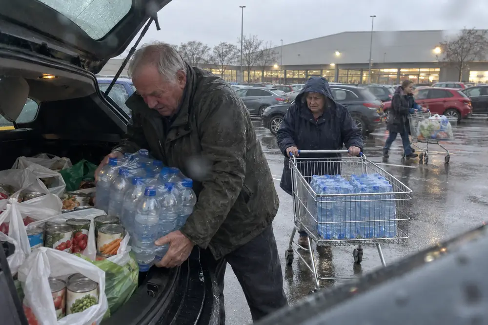 A couple loading bottled water and tins into their car in the rain