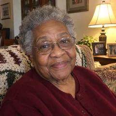Gloria W., a woman in her 70s on her sofa by a lamp