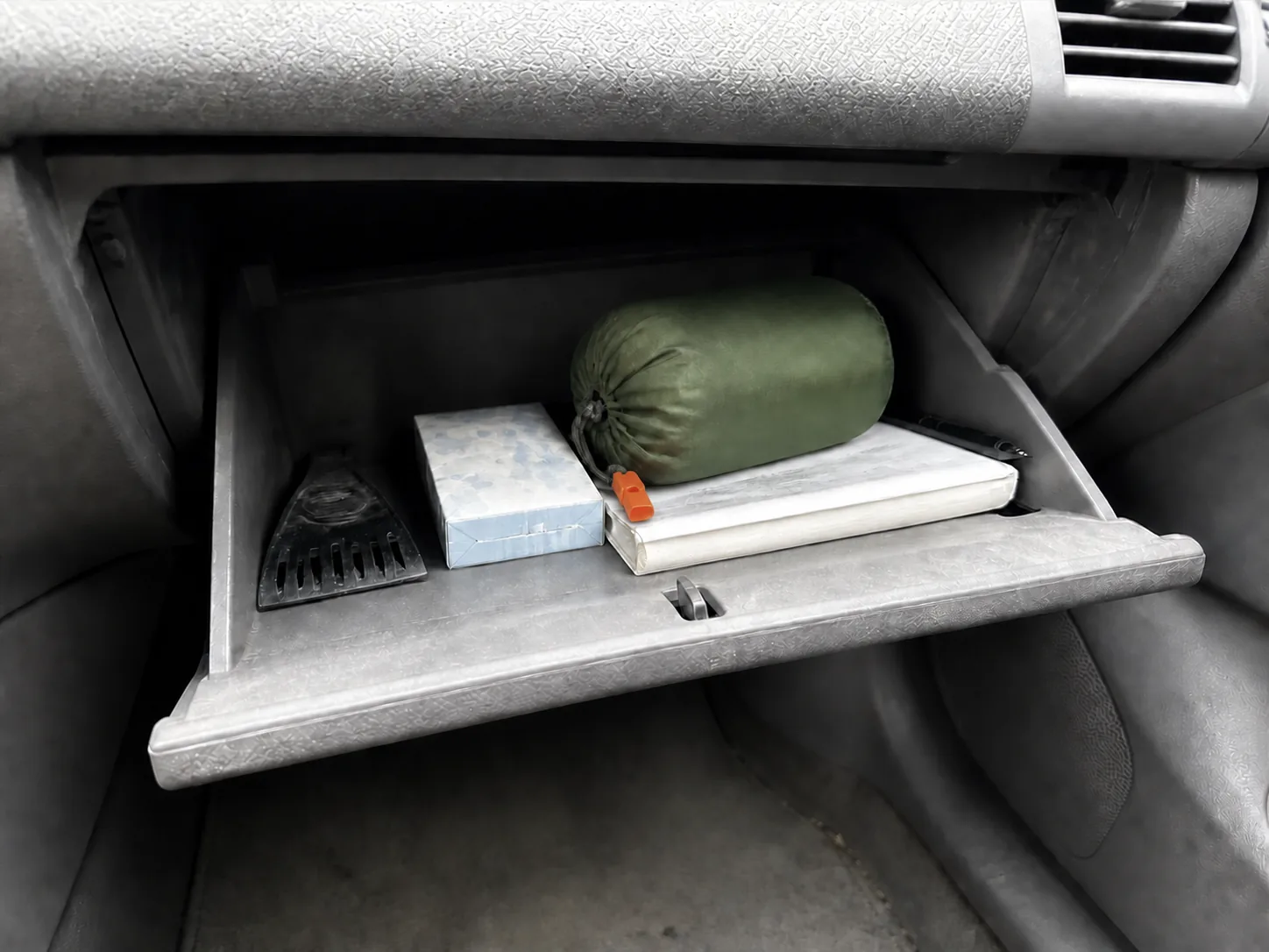 A packed TerraShell lying in an open car glove box beside a box of tissues and an ice scraper