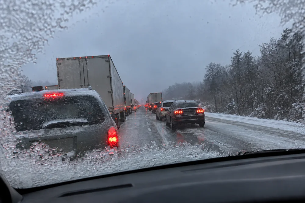 An iced interstate at dusk seen through a frosted windshield: a long line of stopped trucks and cars glazed with ice, the shoulder empty under snow