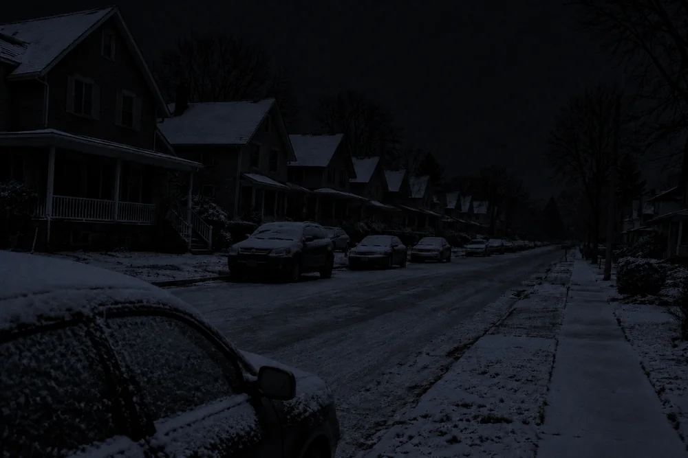 A snowy residential street at night in a blackout, every house on the row dark
