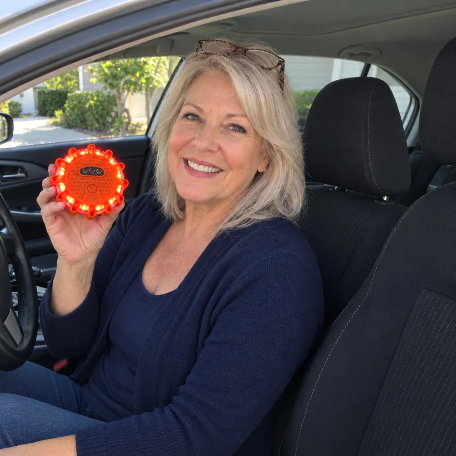 A smiling woman in the driver's seat of her silver car holds up a small orange TerraSignal light, its ring glowing red and amber.
