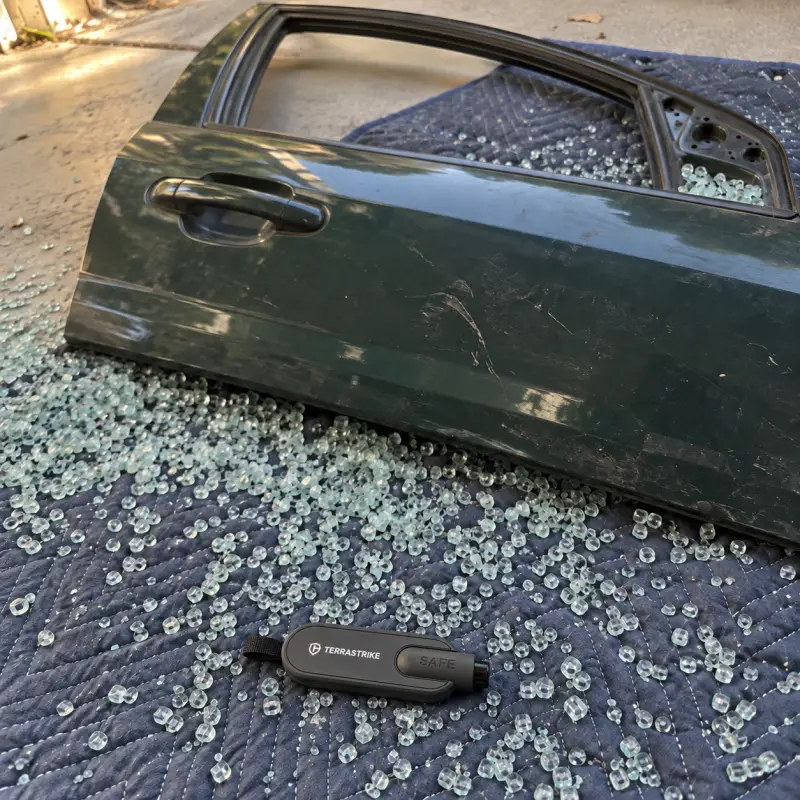 An old car door lies on a garage floor with its side window shattered into small pebbles, a TerraStrike lying beside it.