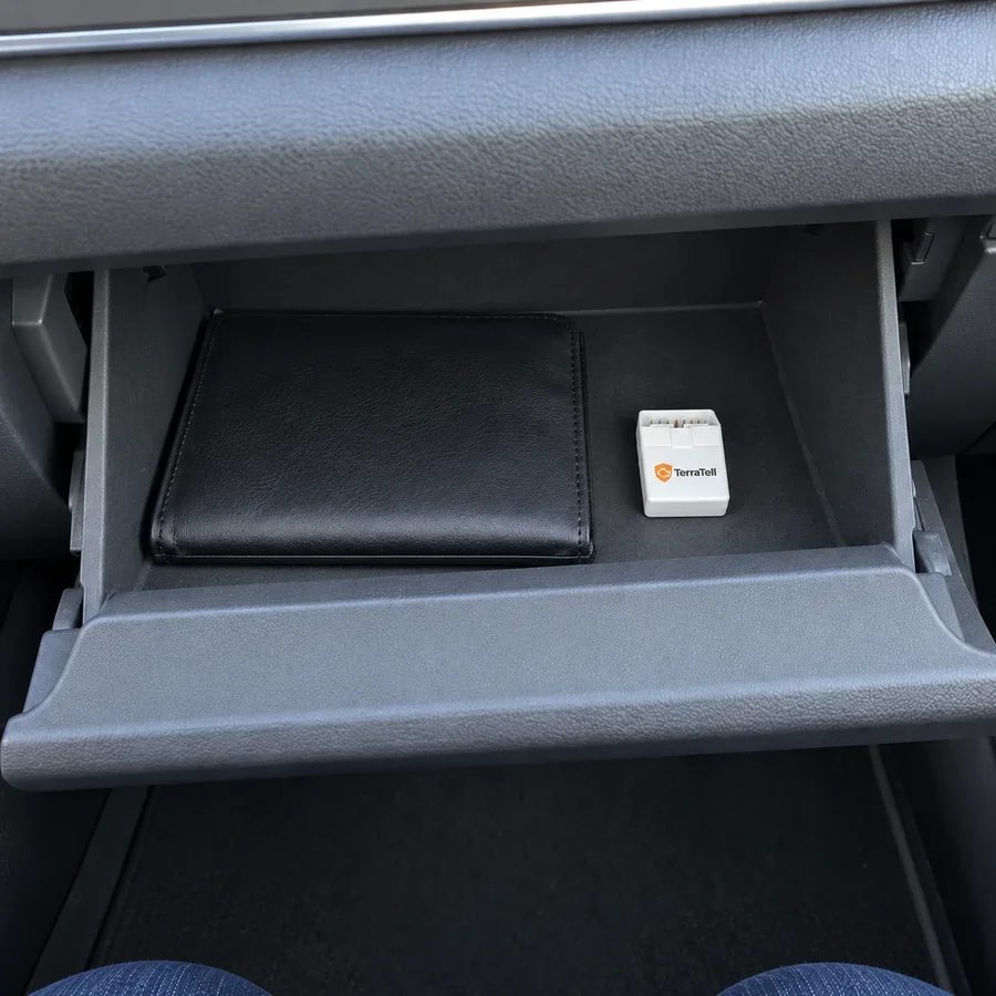 An open glove box in a newer car, the small white TerraTell lying beside the owner's manual.