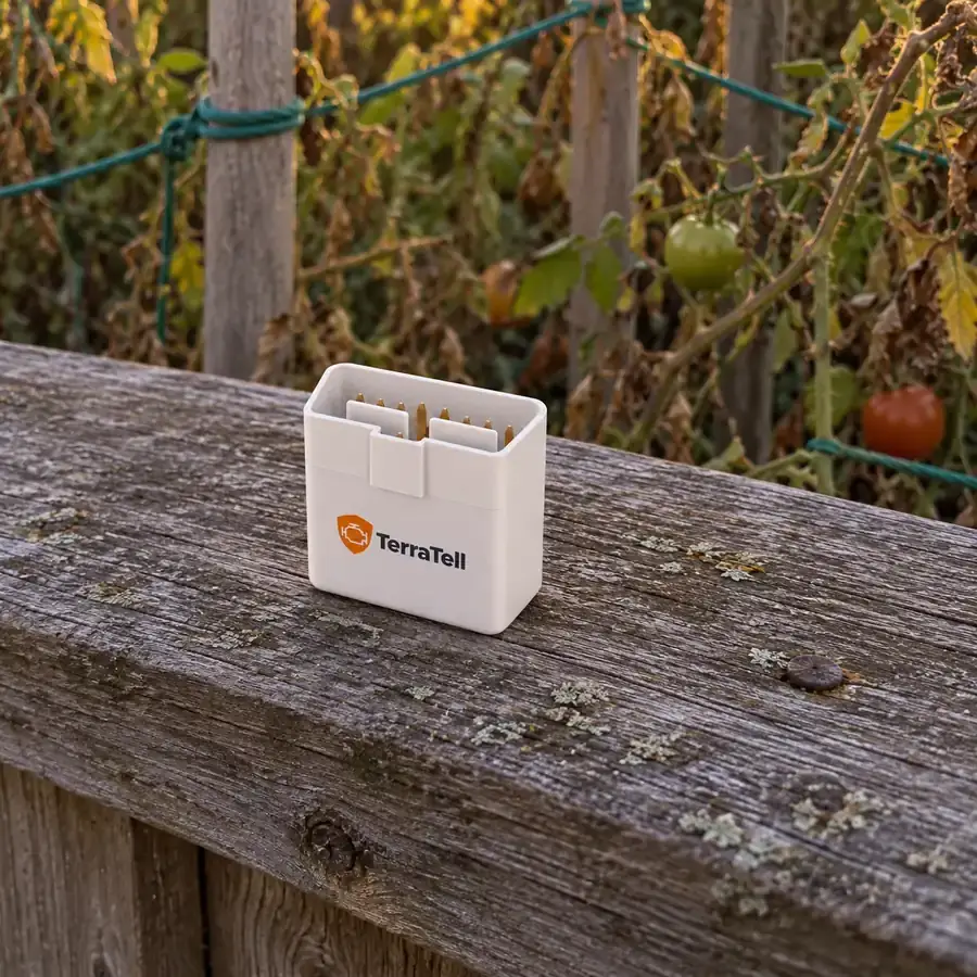 At dusk, the small white TerraTell standing on the top rail of the wooden fence, tomato plants behind it.